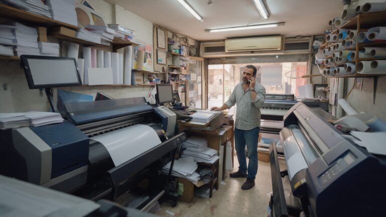 Print shop owner on the phone in his shop full of large printers